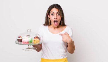 Şok olmuş ve ağzı açık, kendini işaret eden güzel İspanyol bir kadın. Ev yapımı kek konsepti