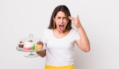 Oldukça İspanyol bir kadın mutsuz ve stresli görünüyor, intihar jesti silah işareti yapıyor. Ev yapımı kek konsepti