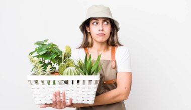 Güzel İspanyol bir kadın omuz silkiyor, kafası karışık ve kararsız hissediyor. Bitkiler ve gargara konsepti