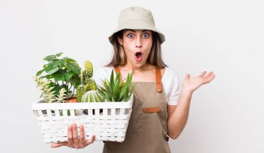 Güzel İspanyol bir kadın şaşırmış ve şok olmuş görünüyor. Çenesi düşmüş ve elinde bir nesne tutuyor. Bitkiler ve gargara konsepti