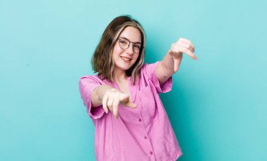 Güzel, beyaz bir kadın mutlu ve kendinden emin, kamerayı iki eliyle gösteriyor ve gülüyor, seni seçiyor.