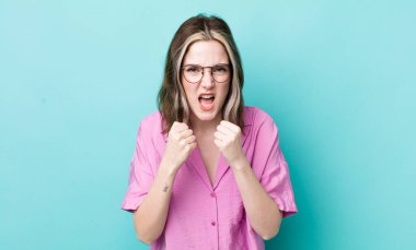 pretty caucasian woman shouting aggressively with annoyed, frustrated, angry look and tight fists, feeling furious