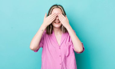 pretty caucasian woman smiling and feeling happy, covering eyes with both hands and waiting for unbelievable surprise