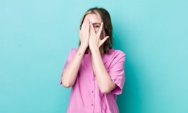 pretty caucasian woman covering face with hands, peeking between fingers with surprised expression and looking to the side