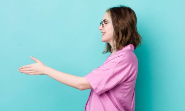 Güzel beyaz bir kadın gülümsüyor, seni selamlıyor ve başarılı bir anlaşma için el sıkışmayı teklif ediyor, işbirliği konsepti.