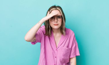 pretty caucasian woman looking bewildered and astonished, with hand over forehead looking far away, watching or searching