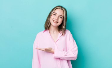 pretty caucasian woman smiling cheerfully, feeling happy and showing a concept in copy space with palm of hand