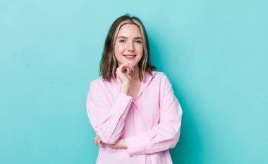 pretty caucasian woman smiling, enjoying life, feeling happy, friendly, satisfied and carefree with hand on chin