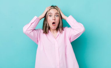 pretty caucasian woman looking excited and surprised, open-mouthed with both hands on head, feeling like a lucky winner