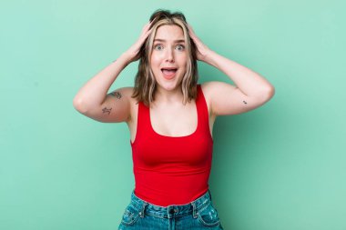 pretty caucasian woman raising hands to head, open-mouthed, feeling extremely lucky, surprised, excited and happy