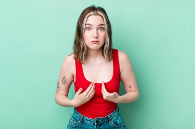 pretty caucasian woman pointing to self with a confused and quizzical look, shocked and surprised to be chosen