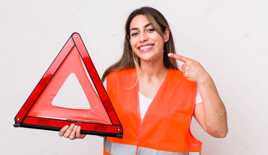 pretty hispanic woman smiling confidently pointing to own broad smile. car triangle concept