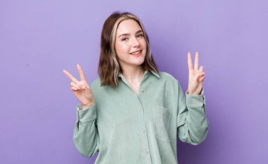 Güzel, beyaz bir kadın gülümsüyor ve mutlu görünüyor, arkadaş canlısı ve tatmin olmuş, zafer ya da barış işareti yapıyor.