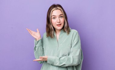 pretty caucasian woman smiling proudly and confidently, feeling happy and satisfied and showing a concept on copy space