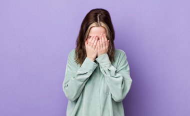 pretty caucasian woman feeling sad, frustrated, nervous and depressed, covering face with both hands, crying