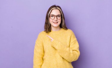 pretty caucasian woman smiling cheerfully, feeling happy and pointing to the side and upwards, showing object in copy space
