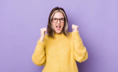 pretty caucasian woman feeling happy, surprised and proud, shouting and celebrating success with a big smile