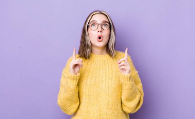 pretty caucasian woman feeling awed and open mouthed pointing upwards with a shocked and surprised look