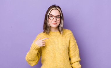 pretty caucasian woman looking proud, confident and happy, smiling and pointing to self or making number one sign