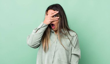 Güzel İspanyol kadın şok olmuş, korkmuş ya da korkmuş görünüyor. Yüzü elle kaplanmış ve parmaklarının arasından gizlice bakıyor.