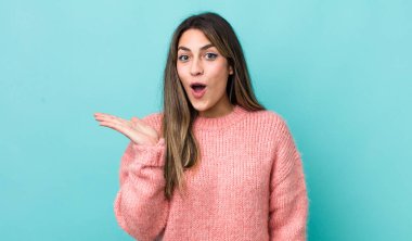 Güzel İspanyol kadın şaşırmış ve şok olmuş görünüyor, çenesi düşmüş, bir objeyi elinde açık bir elle tutuyor.
