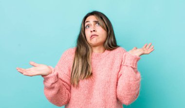 pretty hispanic woman shrugging with a dumb, crazy, confused, puzzled expression, feeling annoyed and clueless