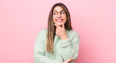 Güzel İspanyol bir kadın mutlu, kendinden emin bir ifadeyle gülümsüyor. Elleri çenesinde, merak ediyor ve yan tarafa bakıyor.