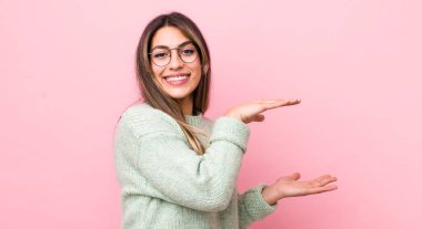 Güzel İspanyol kadın gülümsüyor, mutlu, pozitif ve tatmin olmuş hissediyor, fotokopi alanında nesne ya da konsept tutuyor ya da gösteriyor