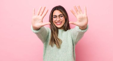 Güzel İspanyol kadın gülümsüyor ve arkadaş canlısı görünüyor, onuncu ya da onuncu numarayı gösteriyor, eli önde, geri sayıyor.