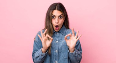 Güzel İspanyol kadın şok olmuş, şaşırmış ve şaşırmış hissediyor. Onaylıyor. İki eliyle işaret veriyor.