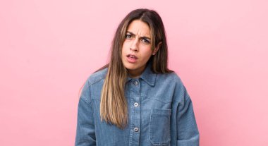 pretty hispanic woman feeling puzzled and confused, with a dumb, stunned expression looking at something unexpected