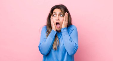 Güzel İspanyol bir kadın mutlu, heyecanlı ve şaşırmış hissediyor, iki eli yüzü üzerinde yana bakıyor.