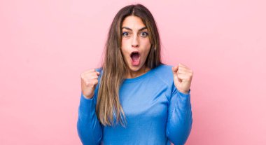 Güzel İspanyol bir kadın kızgın bir ifadeyle agresif bir şekilde bağırıyor ya da yumruklarıyla başarıyı kutluyor.