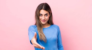 Güzel İspanyol bir kadın gülümsüyor, mutlu, kendinden emin ve arkadaş canlısı görünüyor, bir anlaşmaya varmak için el sıkışmayı teklif ediyor, işbirliği yapıyor.