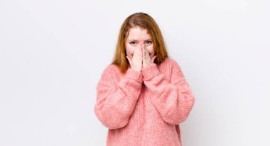 Güzel kızıl saçlı kadın mutlu, şanslı ve şaşkın görünüyor. İki eliyle ağzını kapatıyor.