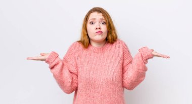 Güzel kızıl saçlı kadın şaşkın ve kafası karışık, şüpheci, farklı seçenekleri tartıyor veya komik bir ifadeyle seçiyor.