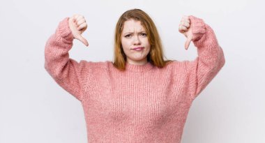 Güzel kızıl saçlı kadın üzgün, hayal kırıklığına uğramış ya da kızgın görünüyor. Anlaşmazlıkta baş parmağını gösteriyor, hayal kırıklığına uğramış hissediyor.