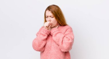 Güzel kızıl saçlı kadın boğazı ağrıyormuş ve grip belirtileri gösteriyormuş. Ağzı kapalı öksürüyormuş.