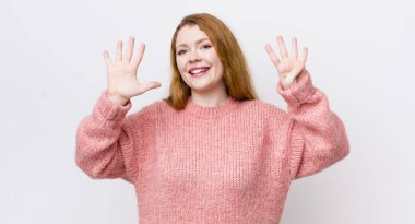 Güzel kızıl saçlı kadın gülümsüyor ve arkadaş canlısı görünüyor. 9 ya da 9 numarayı gösteriyor. Eli önde, geriye doğru sayıyor.