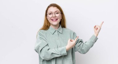 Güzel kızıl saçlı kadın mutlu bir şekilde gülümsüyor ve her iki elinde fotokopi uzayında nesne gösteriyor.