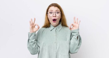 Güzel kızıl saçlı kadın şok olmuş, şaşırmış ve şaşırmış hissediyor. Onayladığını gösteriyor. İki eliyle işaret veriyor.