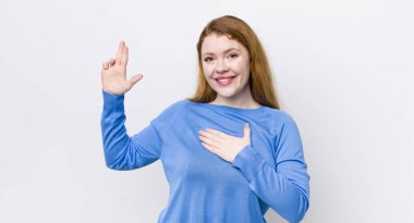 Güzel kızıl saçlı kadın mutlu, kendinden emin ve güvenilir görünüyor, gülümsüyor ve zafer işareti gösteriyor, olumlu bir tavırla.