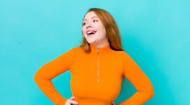 Güzel kızıl saçlı kadın mutlu, neşeli ve kendinden emin görünüyor, gururla gülümsüyor ve iki elini de kalçasında istiyor.