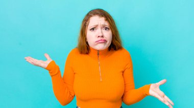 Güzel kızıl saçlı kadın şaşkın, kafası karışık ve stresli görünüyor, farklı seçenekler arasında merak ediyor, kararsız hissediyor.