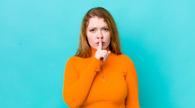Güzel kızıl saçlı kadın ciddi görünüyor ve parmaklarını dudaklarına bastırıp sessizlik ya da sessizlik talep ediyor, sır saklıyor.