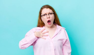 Güzel kızıl saçlı kadın şaşkın, şaşkın ve şaşırmış hissediyor, elleri göğsünde ve ağzı açık, kim olduğunu söylüyor, ben mi??