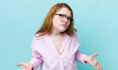 pretty red head woman feeling clueless and confused, having no idea, absolutely puzzled with a dumb or foolish look