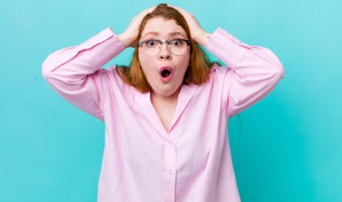 Güzel kızıl saçlı kadın heyecanlı ve şaşırmış görünüyor, ağzı açık, iki eli de başında, kendini şanslı hissediyor.