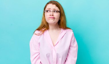 Güzel kızıl saçlı kadın şaşkın ve şaşkın görünüyor, merak ediyor ya da bir sorunu çözmeye çalışıyor ya da düşünüyor.