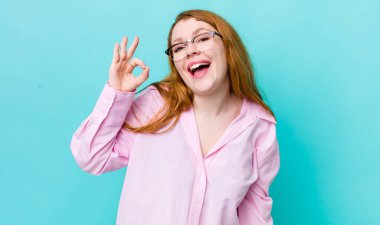 Güzel kızıl saçlı kadın kendini başarılı ve tatmin olmuş hissediyor, ağzı açık gülümsüyor, elle işaret veriyor.